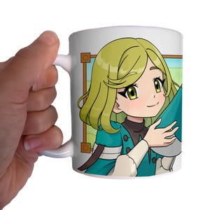 Puede incluir: Taza de cerámica blanca con una colorida ilustración de estilo anime de una chica con cabello verde y ropa verde azulado. La taza está sostenida por una mano, mostrando el diseño y el asa.