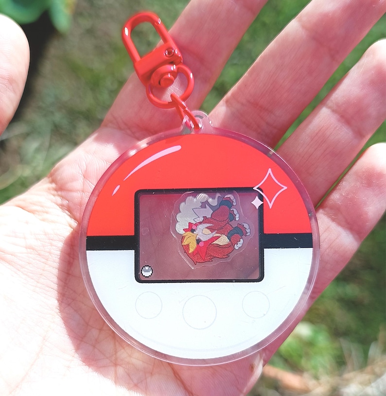 May include: A red and white Pokemon character keychain with a clear plastic casing. The keychain features a red and white Pokeball design with a clear window showing a cartoon image of a red and white Pokemon character.