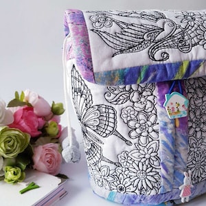 May include: A white drawstring bag with a black and white embroidered design of butterflies, flowers, and birds. The bag has a purple, pink, and blue tie-dye pattern on the bottom and top edges.