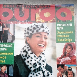 May include: A Burda magazine cover featuring the text "burda" in large red letters. The cover displays various fashion photography images, including a person wearing a white and black spotted faux fur hat and scarf, and other models.