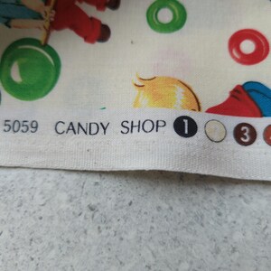May include: Fabric with a whimsical candy shop theme. The design features illustrations of children, candy, and the words "CANDY SHOP". The color palette includes red, green, yellow, and blue on a cream background. The fabric is likely cotton or a similar material.