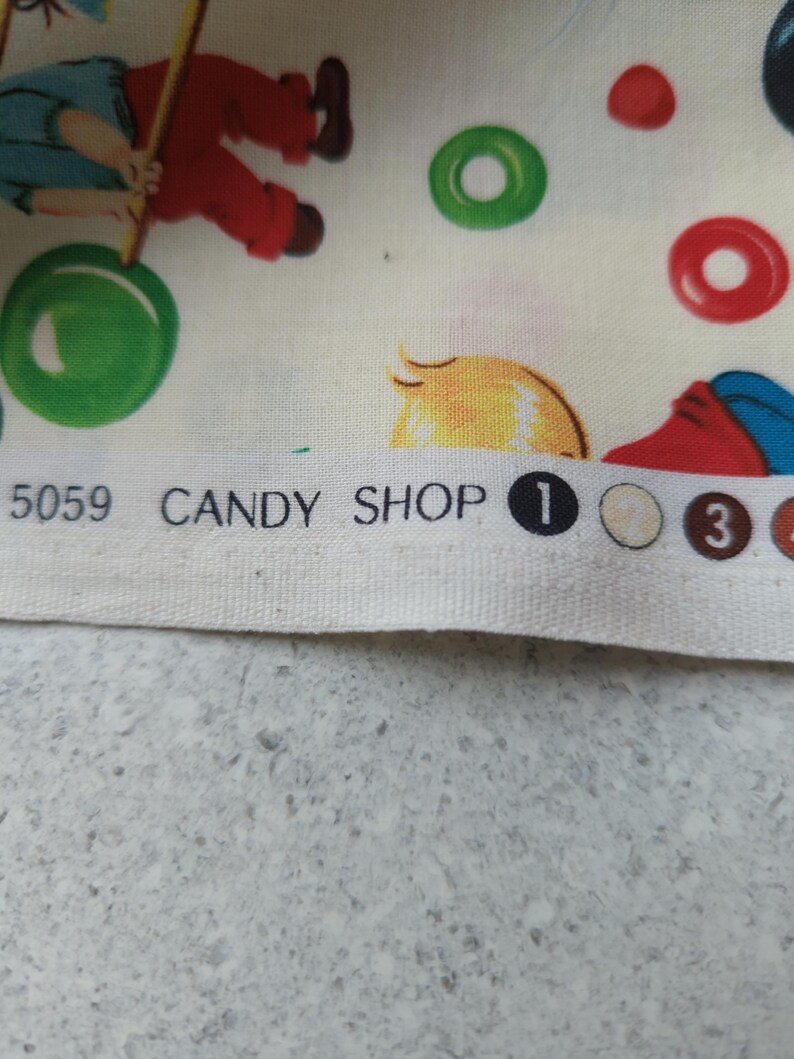 May include: Fabric with a whimsical candy shop theme. The design features illustrations of children, candy, and the words "CANDY SHOP". The color palette includes red, green, yellow, and blue on a cream background. The fabric is likely cotton or a similar material.