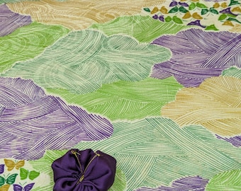 May include: A vibrant fabric with a repeating pattern of stylized clouds in shades of green, purple, and tan. A small, dark purple, drawstring pouch is in the foreground. The fabric design has a textured, hand-drawn appearance.