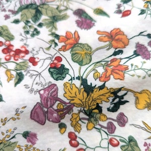 Puede incluir: Una tela blanca con un patrón floral que presenta varias flores, hojas y bayas en tonos de rojo, naranja, amarillo, verde y morado.