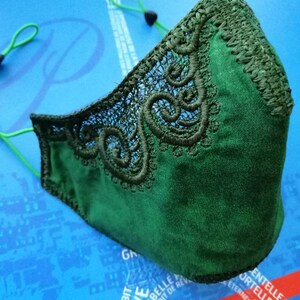 May include: A dark green face mask with a delicate lace trim. The mask has elastic ear loops.