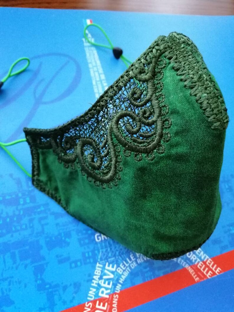 May include: A dark green face mask with a delicate lace trim. The mask has elastic ear loops.