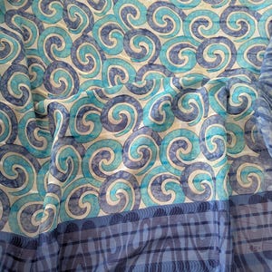 May include: A sheer fabric with a repeating pattern of blue and teal swirls. The fabric has a border of blue and navy blue stripes. The fabric is lightweight and appears to be silk or a similar material.
