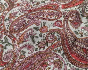 May include: Close-up of a fabric with a paisley pattern. The design features large, teardrop-shaped motifs in shades of red, pink, and brown, set against a cream-colored background. Small floral elements are interspersed throughout the pattern.