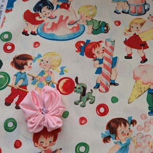 May include: A pink fabric flower with a beaded center sits atop a vintage-style fabric featuring children enjoying treats. The fabric has a repeating pattern of cartoon children, ice cream, and candy on a cream background with red and green accents.