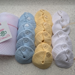 May include: A collection of reusable nursing pads in various colors: light blue, yellow, and white. Each pad is round with a button closure. A mesh bag with a tag that reads "Folina Di" is also present.
