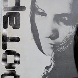 Puede incluir: Portada de álbum vintage con un retrato en escala de grises de una mujer. La palabra "Sofia" está impresa en una fuente pixelada. Un disco de vinilo negro es parcialmente visible.