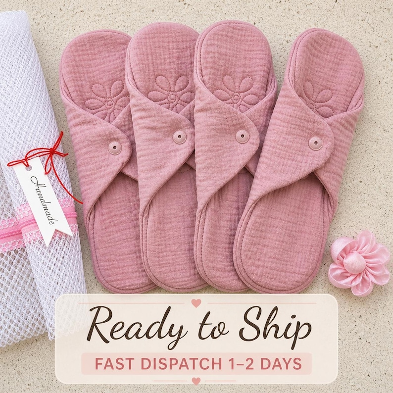 May include: Four reusable cloth menstrual pads in a dusty rose color, each featuring a quilted flower pattern and a single snap closure. A white mesh laundry bag with a tag labeled Handmade and a small pink fabric flower are positioned nearby.