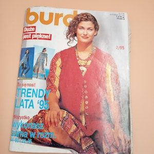 May include: A magazine cover featuring a woman wearing a red vest and a patterned skirt. The magazine is titled "Burda" and the text "Trendy Lata '95" is visible. The cover also features the text "Duze jest piekne!" and "To sie nosi!"