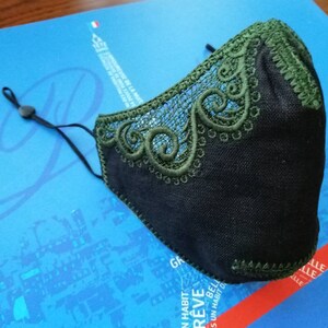 May include: Black face mask with green lace trim. The lace has a delicate floral pattern. The mask has a black elastic strap.