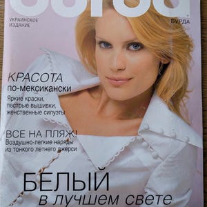 Op de afbeelding: Een tijdschriftomslag met een blonde vrouw met blauwe ogen die een wit overhemd draagt. De tijdschrifttitel "burda" staat bovenaan, met tekst in het Russisch. De cover bevat de tekst "БЕЛЫЙ в лучшем свете" en "Новый образ для нового сезона".