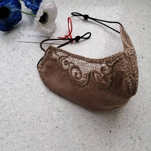 May include: A beige face mask with delicate lace detailing and black elastic ear loops. The mask has a tag that says "remarkable" on it.