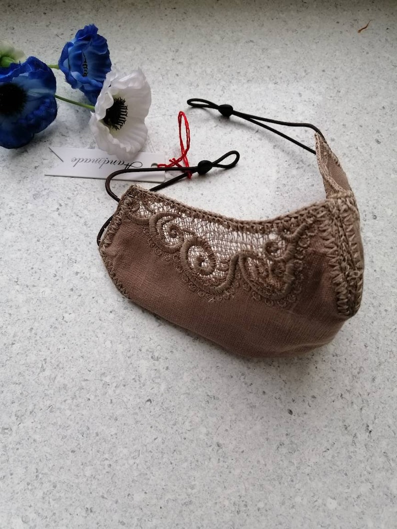 May include: A beige face mask with delicate lace detailing and black elastic ear loops. The mask has a tag that says "remarkable" on it.
