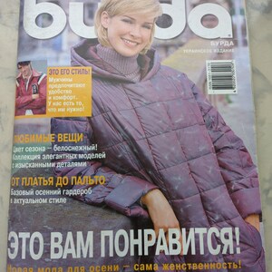 May include: A magazine cover featuring a woman wearing a purple quilted jacket. The magazine is titled "Buda" and the text "This will please you!" is printed in large white letters. The magazine is a Ukrainian publication and the issue number is 10/2002.