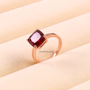 May include: A rose gold ring featuring a large, square-shaped, red gemstone.