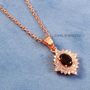 May include: A rose gold necklace with a pendant featuring a large oval-shaped brown gemstone surrounded by smaller clear gemstones. The pendant is in the shape of a flower with a pointed bottom.