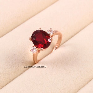 Peut inclure: Une bague en or rose avec une grande pierre rouge ovale entourée de petites pierres blanches.