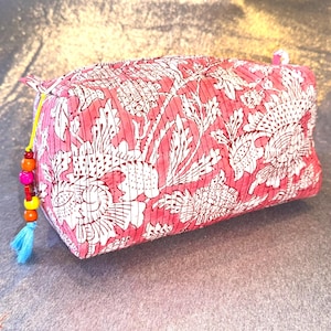 Puede incluir: Una bolsa de maquillaje de estampado floral rosa con un borla azul y cuentas de colores.