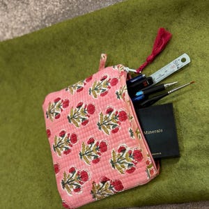 May include: Pink quilted zippered pouch with a floral print. The pouch is open and contains a ruler, pens, paintbrushes, and a small black notebook with the word "Minerals" printed on the cover.