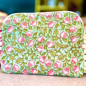 May include: A green and pink floral print quilted makeup bag with a white zipper.