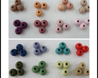 May include: Assortment of wooden beads in various colors, including brown, beige, purple, pink, blue, teal, red, green, and light green. The beads are arranged in groups of three on a white surface.