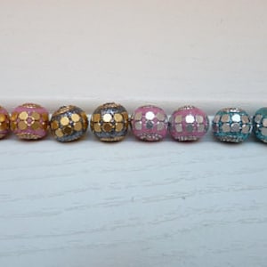 Könnte beinhalten: Acht runde Perlen mit glitzerndem Finish. Die Perlen sind in vier verschiedenen Farben: Gold, Rosa, Silber und Türkis.