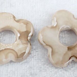 May include: Two flower-shaped decorative objects with a hole in the center. The objects are a light beige color with darker brown marbling. They have a glossy finish and are set against a white background.