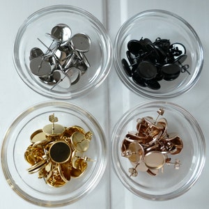 Op de afbeelding: Vier glazen kommen met oorsteker-vondsten. De kommen zijn gerangschikt in een 2x2 raster. De vondsten zijn in vier verschillende kleuren: zilver, zwart, goud en rosé goud.