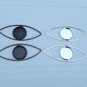 May include: Two pairs of silver and bronze eye-shaped metal settings for crafting. Each setting has a round, flat, open center for adding a cabochon.