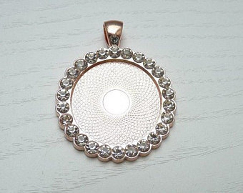 May include: Rose gold pendant with a clear round bezel and a border of clear rhinestones.