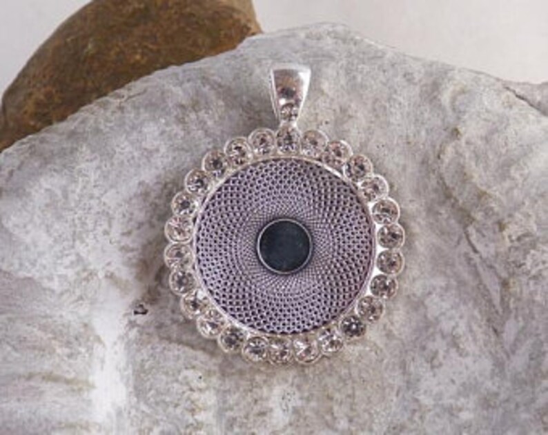 May include: Silver pendant with a round, clear crystal-encrusted frame and a blank center for customization.