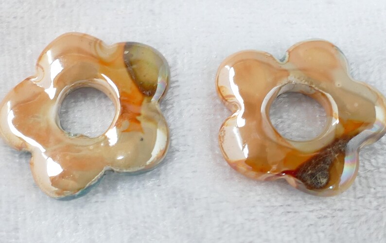 May include: Two flower-shaped beads with a hole in the center. The beads have a glossy finish with shades of orange, brown, and cream. The beads are likely made of glass or a similar material.