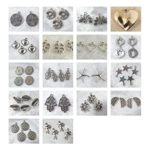 Könnte beinhalten: Eine Sammlung silberfarbener Anhänger in verschiedenen Formen, darunter Herzen, Sterne, Blumen und Münzen. Die Anhänger sind für die Schmuckherstellung und das Basteln bestimmt. Die Aufnahme erfolgt von oben.