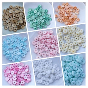 Può includere: Assortimento di perline rotonde colorate con un motivo a righe. Le perline sono disposte in file su piatti bianchi. I colori includono marrone, verde, arancione, azzurro, rosa, bianco e azzurro.