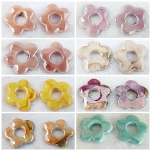 May include: A collection of flower-shaped ceramic beads in various colors, including pink, yellow, and blue. Each bead has a hole in the center, suitable for jewelry making or crafts. The beads have a glossy finish.