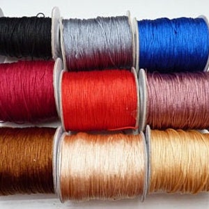 Könnte beinhalten: Sortiment von Spulen mit gewachstem Garn in verschiedenen Farben, darunter Schwarz, Grau, Blau, Rot, Braun, Rosa und Beige.