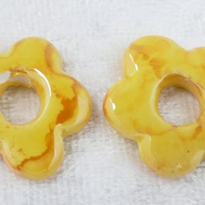 May include: Two yellow flower-shaped beads with a glossy finish. The beads have a hole in the center and a marbled effect with brown and orange hues. These beads are suitable for jewelry making.