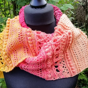 May include: A crocheted infinity scarf in shades of orange, pink, and red. The scarf is made with a variety of stitches, creating a textured and intricate design.