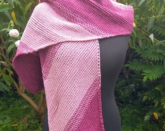 May include: A handmade, knitted scarf in shades of pink and purple is draped over a black mannequin. The scarf features a diagonal color block design, with a lighter pink on one side and a deeper purple on the other. The texture of the knit is visible.