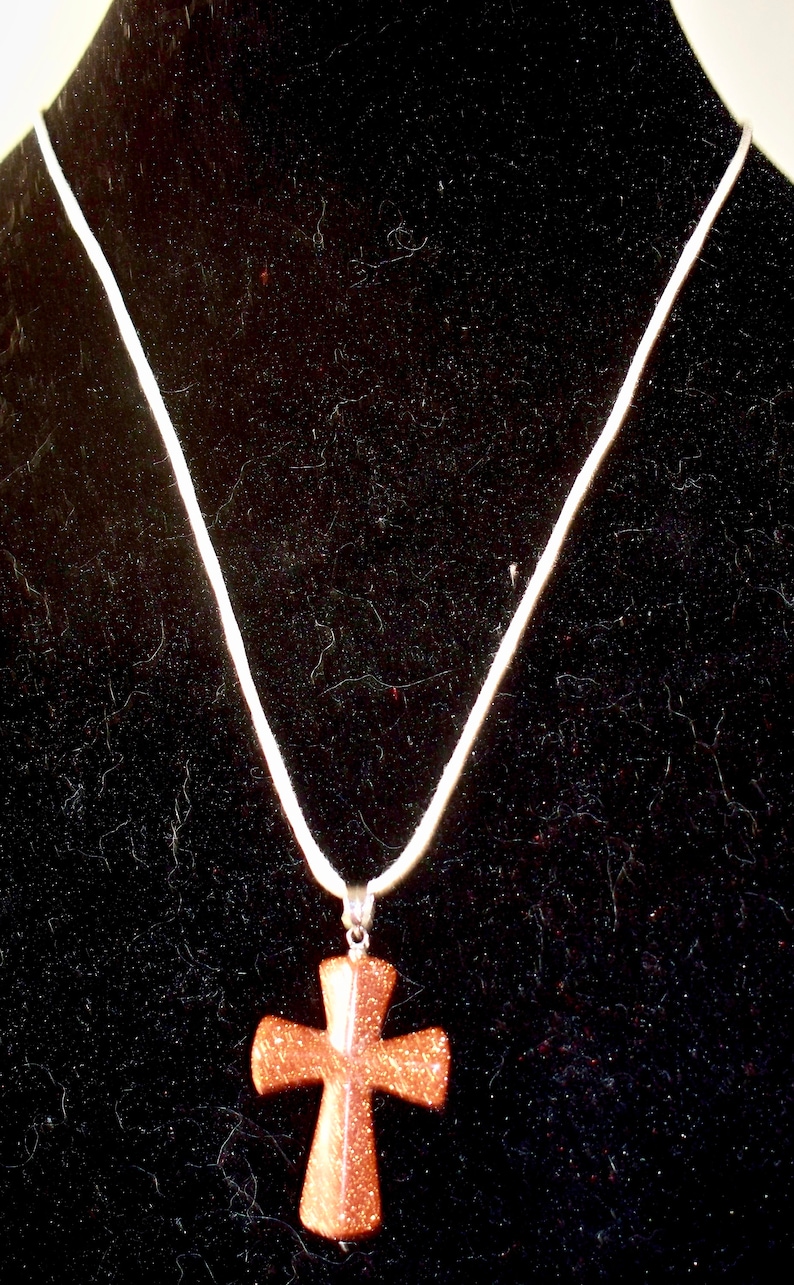 Carved Goldstone cross on cotton cord