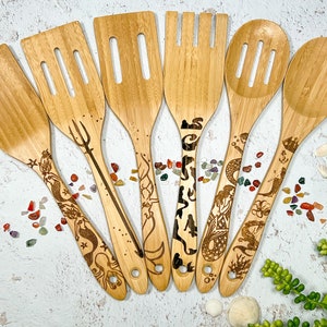 May include: Set of seven wooden kitchen utensils with mermaid and ocean-themed designs. The utensils include a slotted spoon, a spatula, a spoon, a fork, and three spatulas.