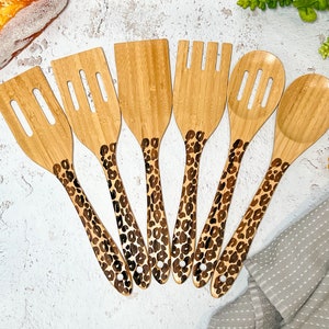 May include: Set of seven wooden kitchen utensils with leopard print handles. The utensils include a slotted spoon, a solid spoon, a spatula, a slotted spatula, and a fork.