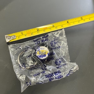 May include: A new "Show Ring Key Ring" in its original packaging. The key ring is silver-colored and has a circular design. The packaging is clear plastic with blue text and a yellow measuring tape is next to it.