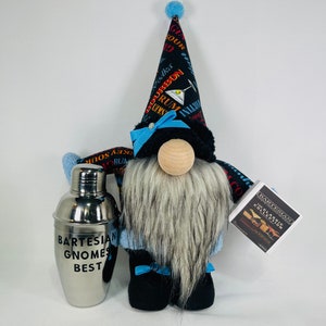 May include: A gnome wearing a black and blue hat with a cocktail print and a blue and white bow. The gnome has a long white beard and is holding a silver cocktail shaker that says "Bartesian Gnomes Best".