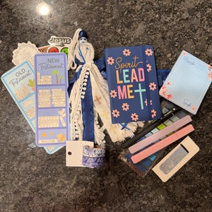 K&ouml;nnte beinhalten: Ein Set aus Schreibwaren, bestehend aus einem blauen Notizbuch mit dem Text Spirit Lead Me, einem Lesezeichen f&uuml;r das Neue Testament, einem Notizblock mit Blumenmuster, zwei Rollen Washi-Tape, einer Quaste sowie Stiften in Rosa und Blau.