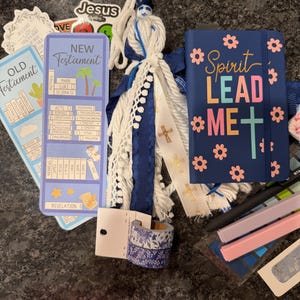 K&ouml;nnte beinhalten: Eine Sammlung von Gegenst&auml;nden, darunter ein blaues Notizbuch mit dem Text Spirit Lead Me, ein Lesezeichen f&uuml;r das Neue Testament, eine Quaste mit wei&szlig;en und blauen B&auml;ndern, zwei Rollen florales Washi-Tape und Aufkleber mit religi&ouml;sem Text.